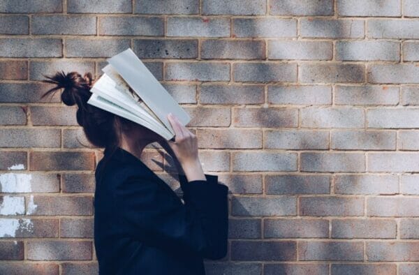 勉強しなければいけないのに勉強する気になれず本で顔を覆って上を向いている女の子のイメージ